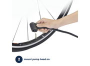 A hand is attaching a black bicycle pump hose to a valve on a tire mounted on a wheel, with instructional text at the bottom reading '2 mount pump head on.'.
