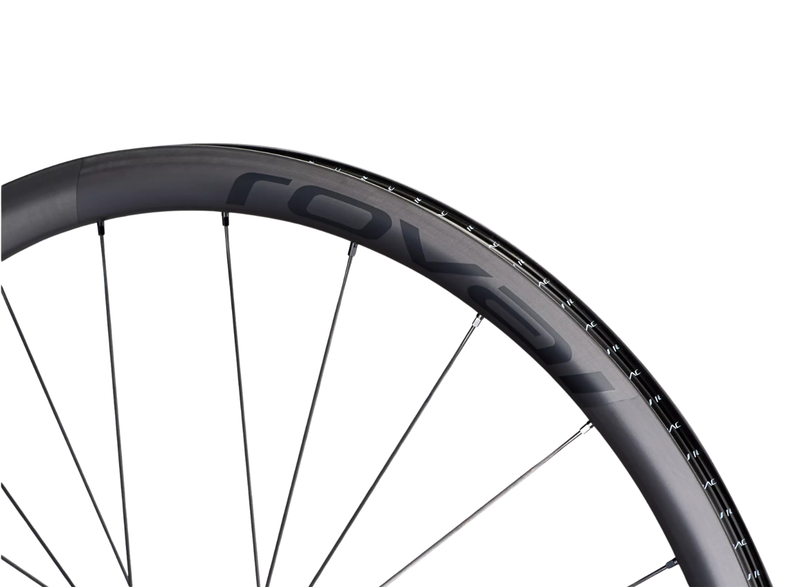 A close-up of the Roval Alpinist CLX II carbon wheelset shows its slim metal spokes and subtle branding on the tubeless-ready rim, set against a white background.