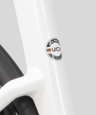Close-up of a white bicycle frame with a circular UCI World Team sticker, next to a black tire, on a light gray background.