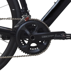 Close-up of a bicycle crankset with a black chainring, silver chain, and black pedal arm against a white background.